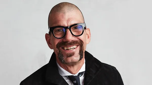 A person with a mustache smiles in a corporate headshot.