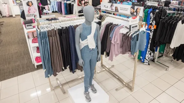 A store mannequin dressed in workout clothes stands in front of a rack of apparel.