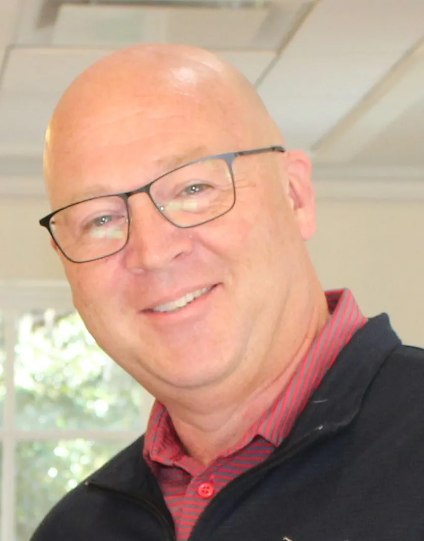 A head and shoulders photo of a person om a room with white walls.