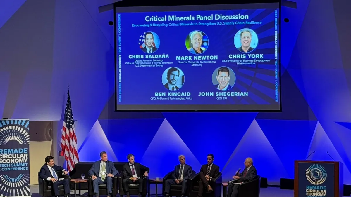speakers sit on a stage with a projection screen above them