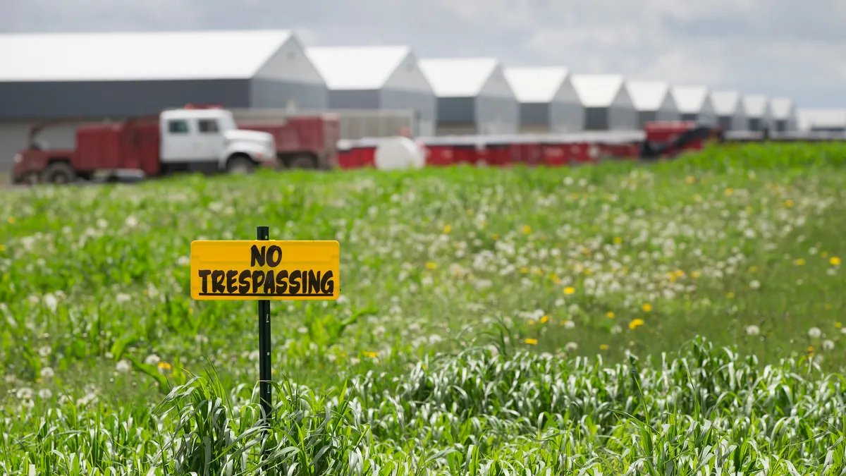 No trespassing sign seen on a farm field with chicken coops in the background