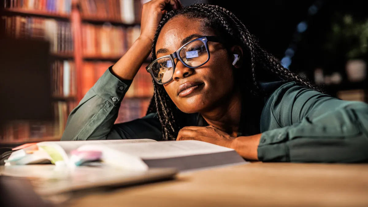 A young college student looks at a textbook in a library.