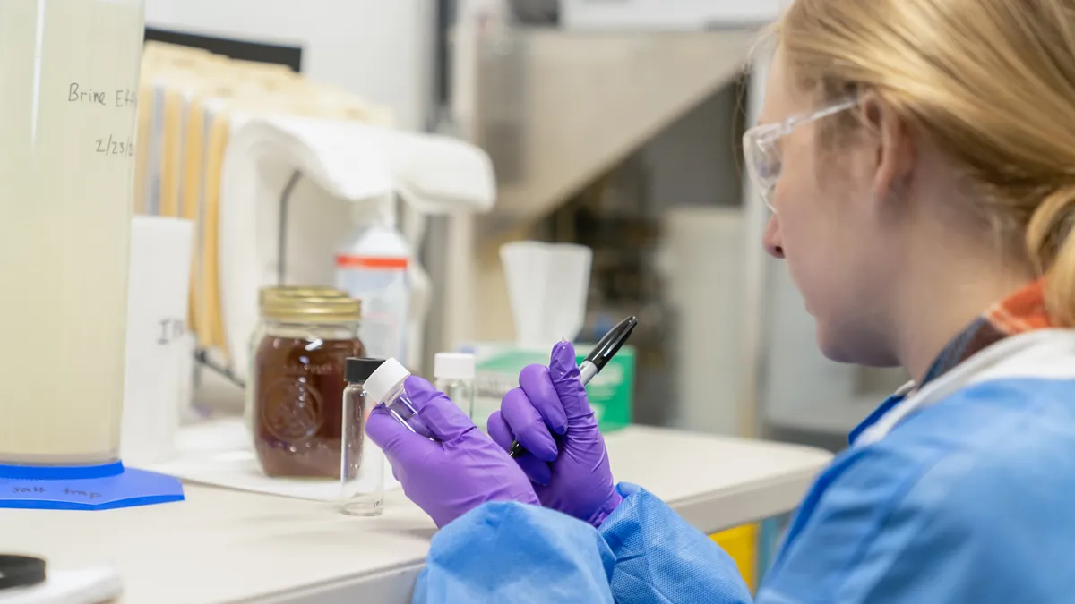 A woman writes on a beaker in a lab