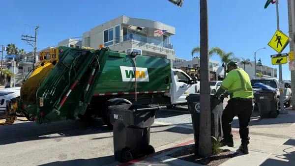A worker rolls a trash cart to a trash truck on the street