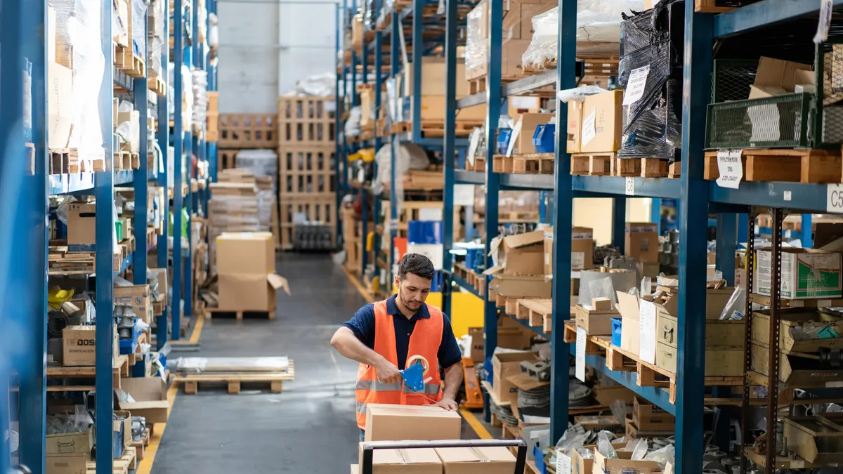 Man warehouse worker sealing a box with adhesive tape for delivery