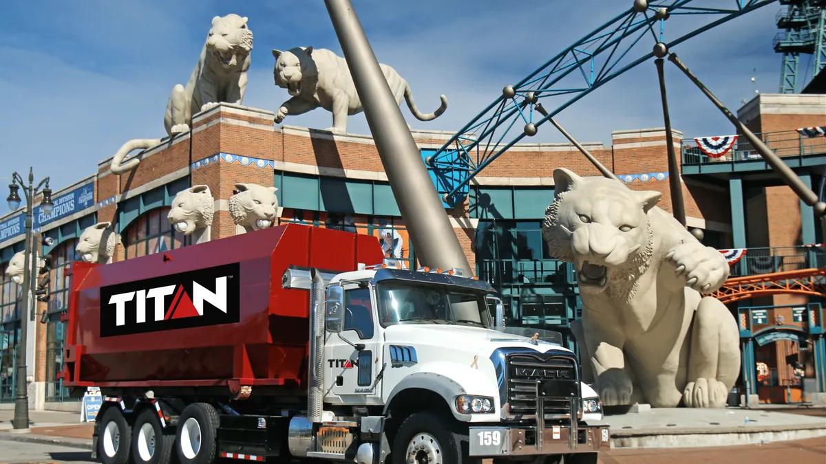 A red waste truck with the Titan Environmental logo in front of a stadium with tiger statues