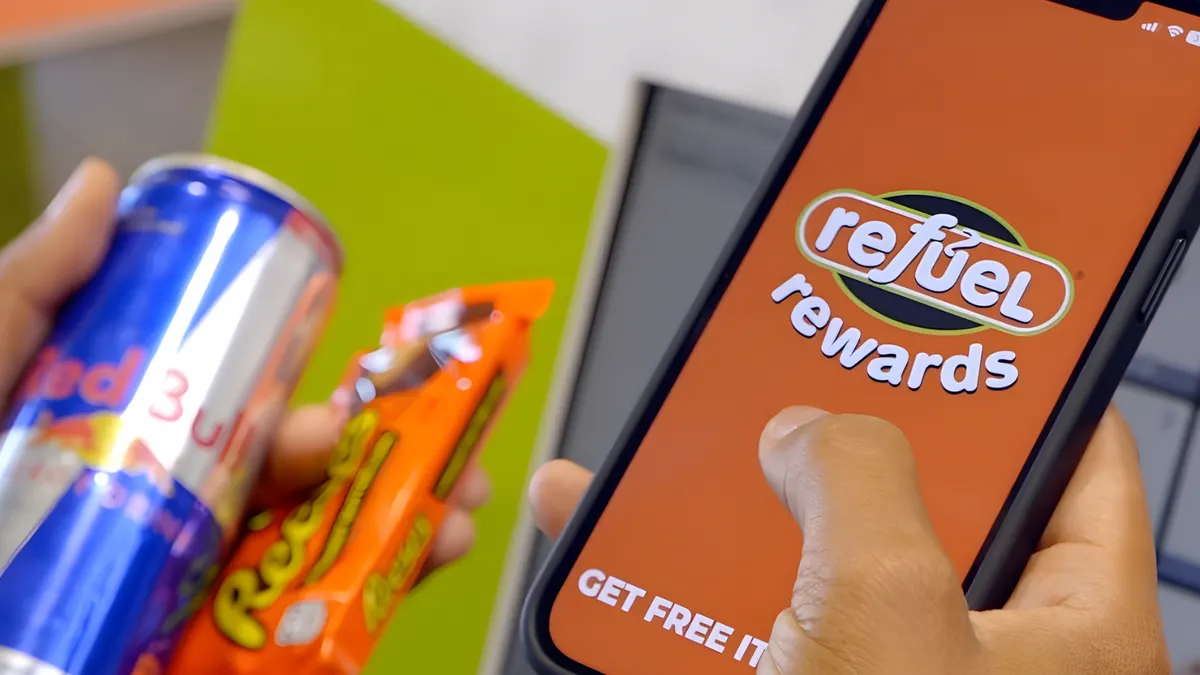 A photo of a hand holding a cell phone. Text on the phone screen says Refuel Rewards Get Free Items