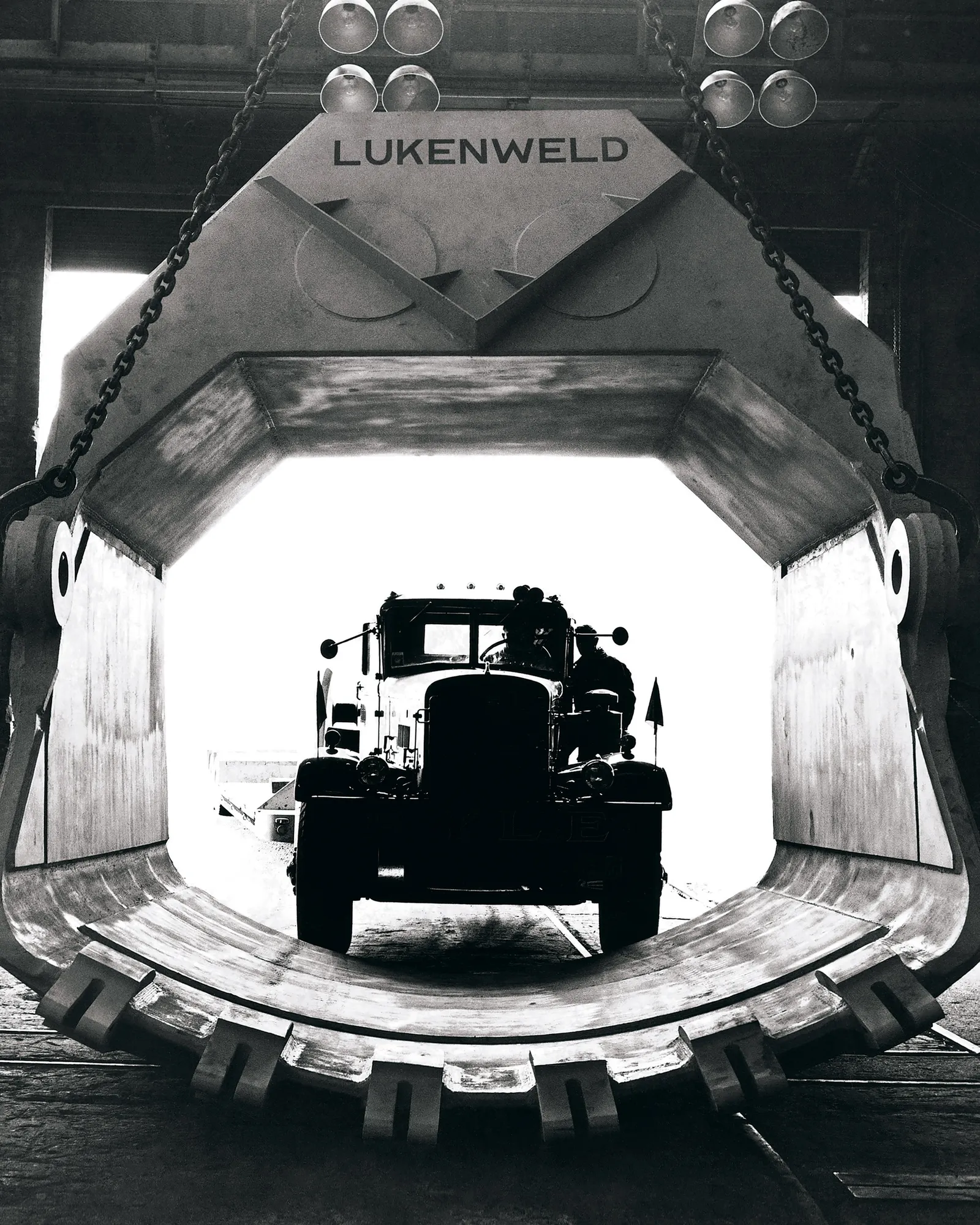 A black n white photo of a truck entering a lift. The top of the lift reads, “Lukenweld.”