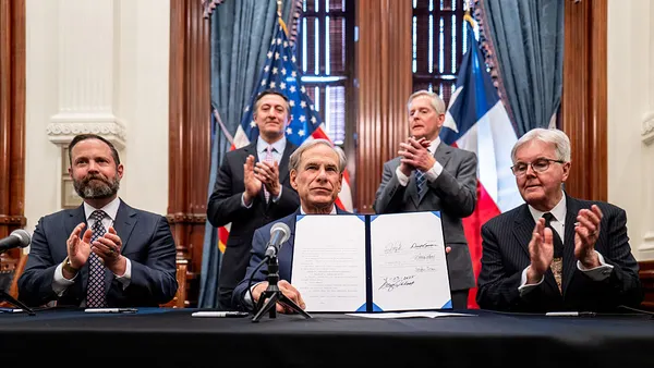 Texas Gov. Greg Abbott is seen sitting at a desk surrounded by men