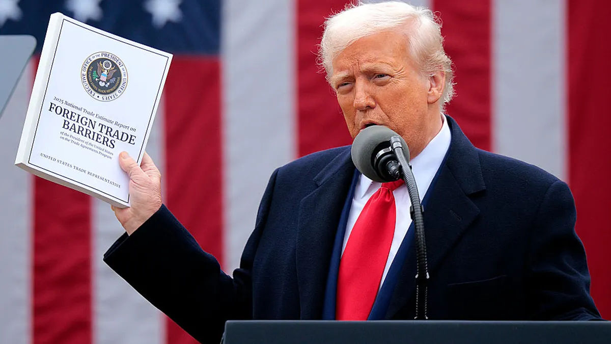 Donald Trump holds up a pamphlet that says "Foreign Trade Barriers" while speaking at a podium.