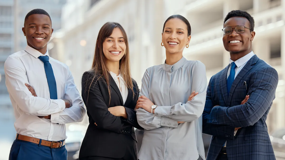 A group of four lawyers stands next to one another outside in a city while smiling