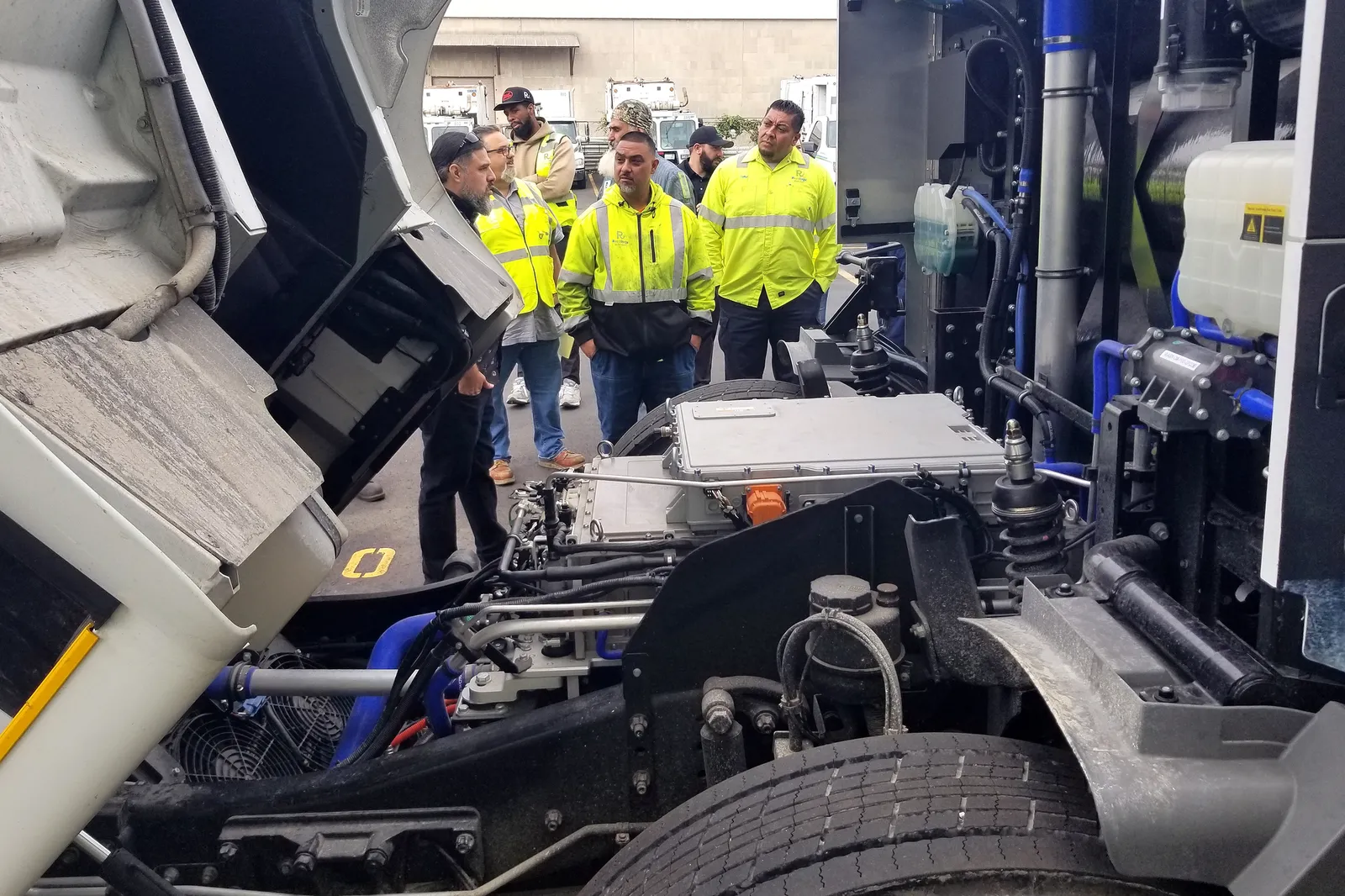 People in high-visibility jackets inspect a power system sitting between the trailer and cab of a heavy-duty truck.