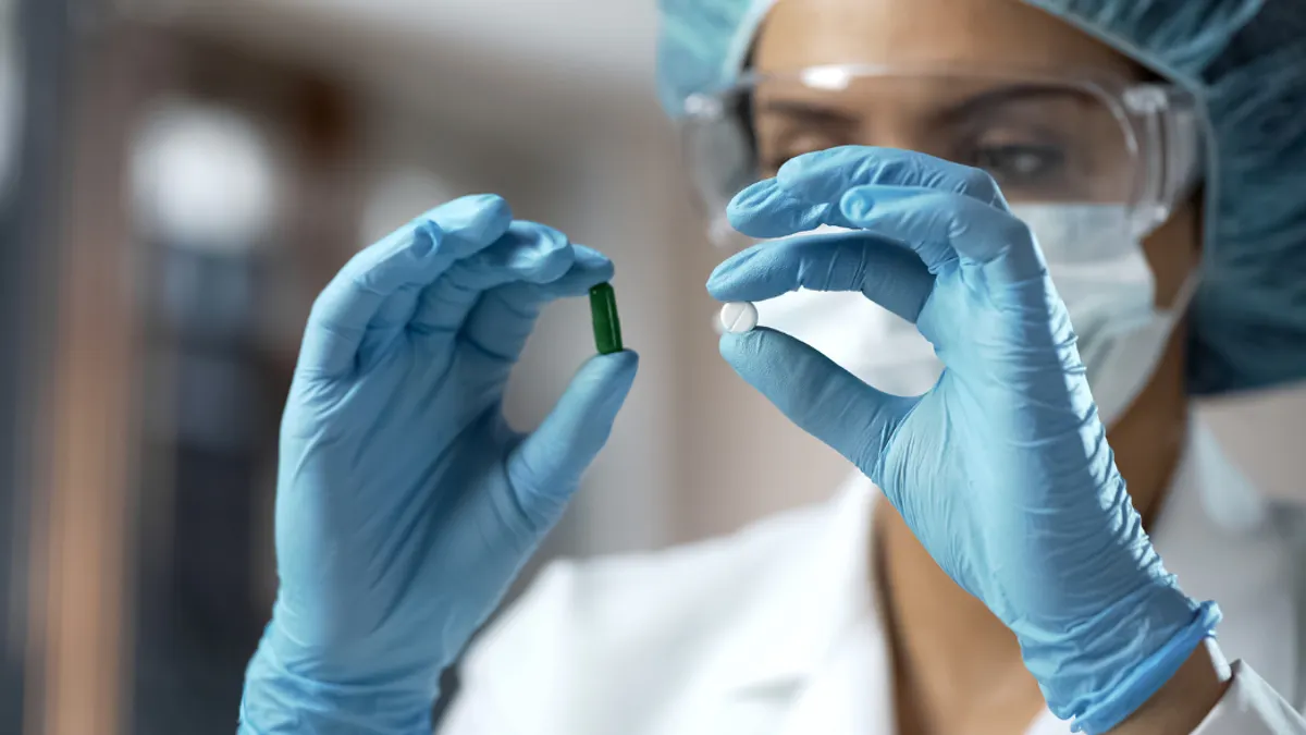 Woman in lab coat and gear analyzing two different pill medicines.
