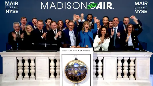 A group of people clapping and cheering on an elevated balcony with a brass bell on front of the balcony.