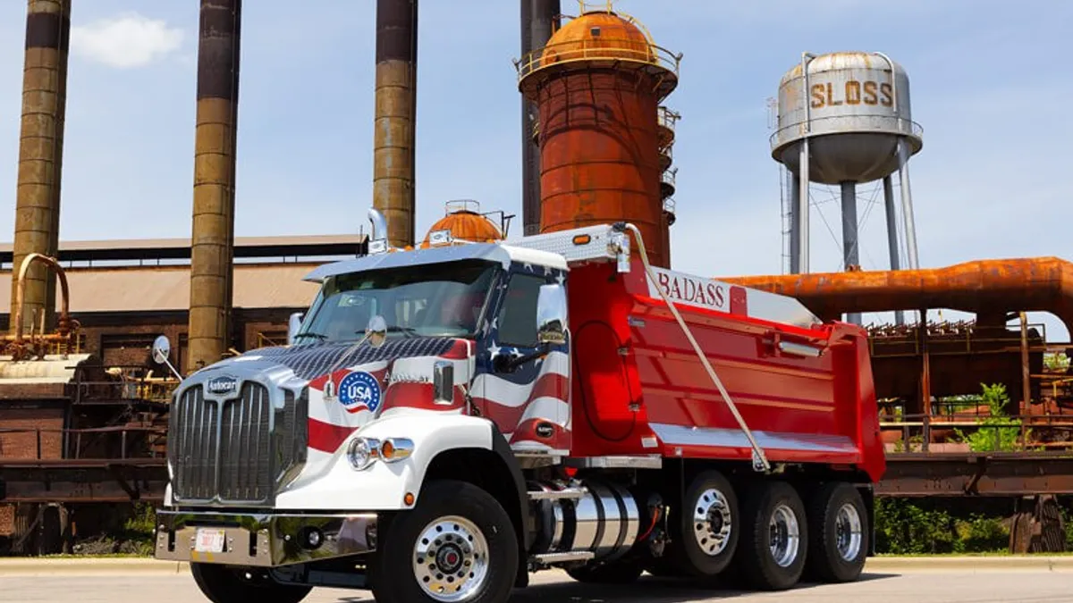 A red and white dump truck parked in front of a rusty Sloss factory