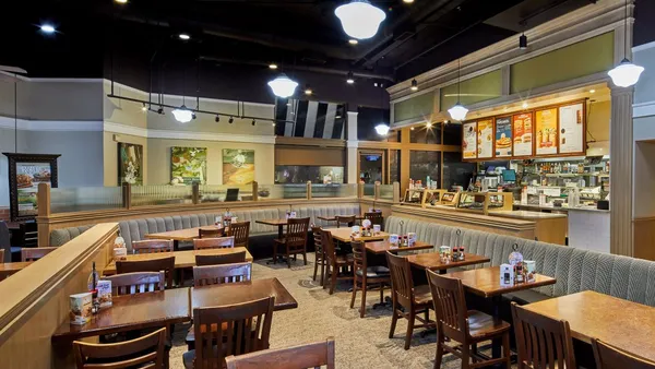 A photograph of the inside of a Corner Bakery with chairs and booths in the foreground and ordering counter in the background.