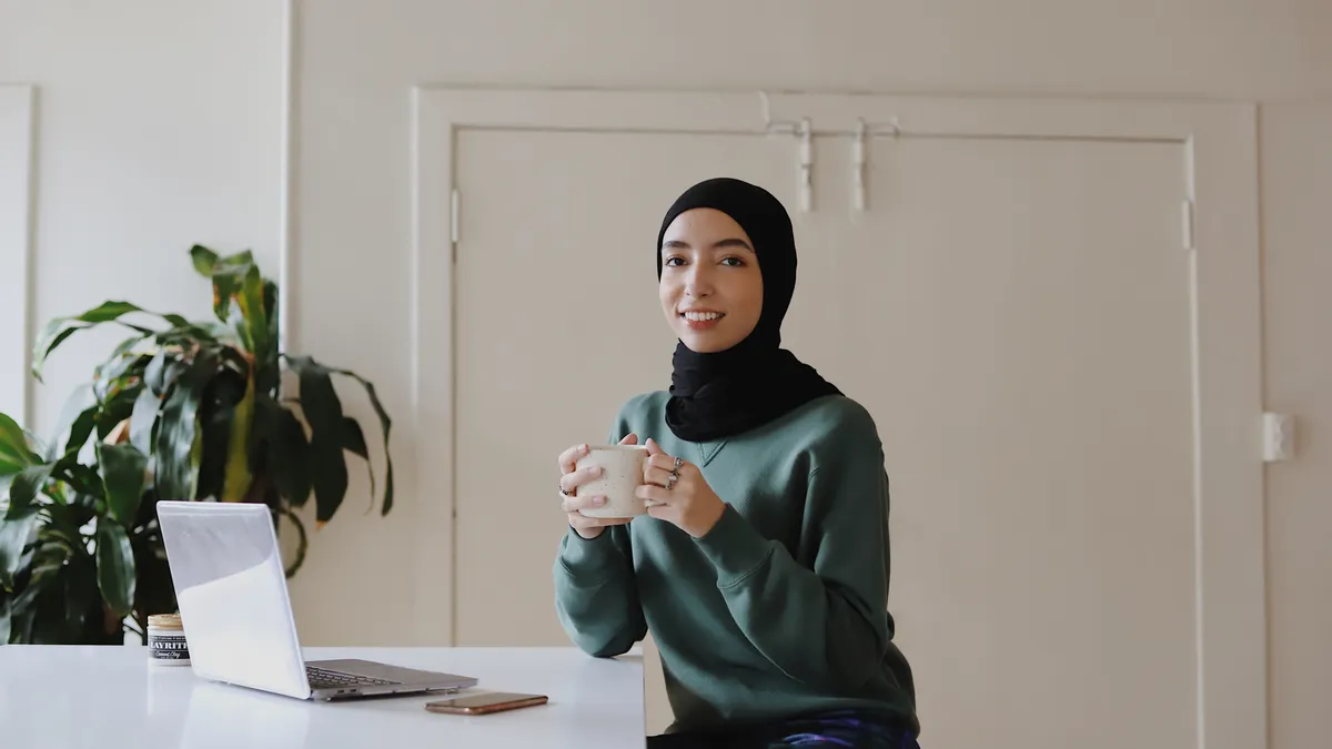 A hijabi person with a laptop looks at the camera