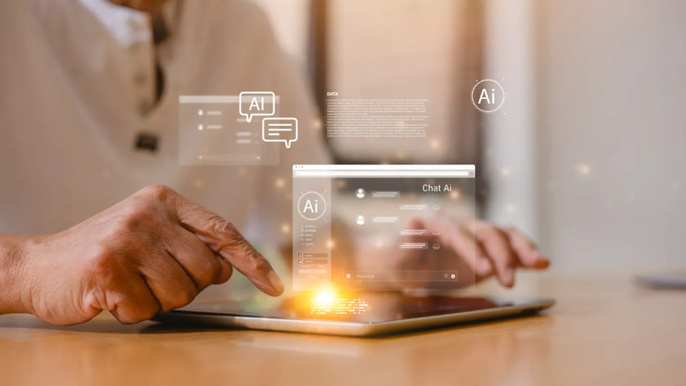 A person using a tablet at a table with icons that say AI superimposed over the image.