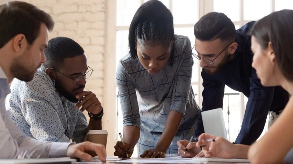 A group of people huddle around a paper on a table.