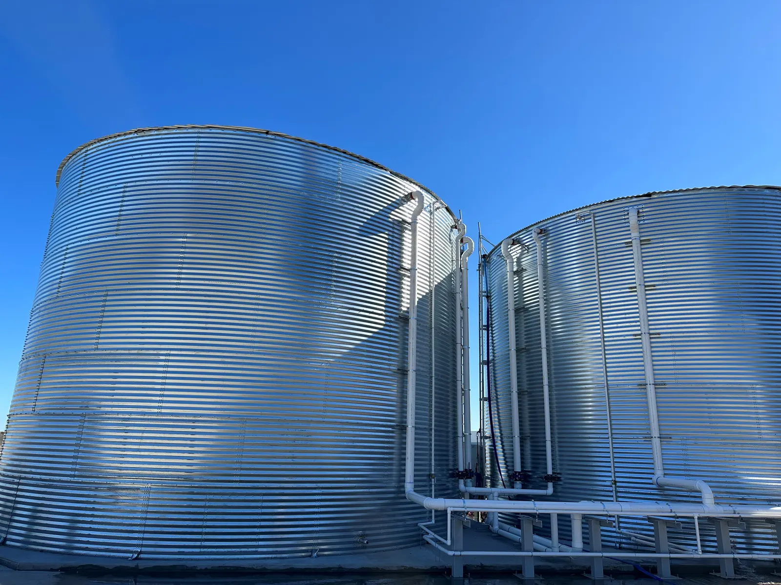 Two large silver metal tanks for collecting rainwater to be used as beverages with a blue sky in the background.