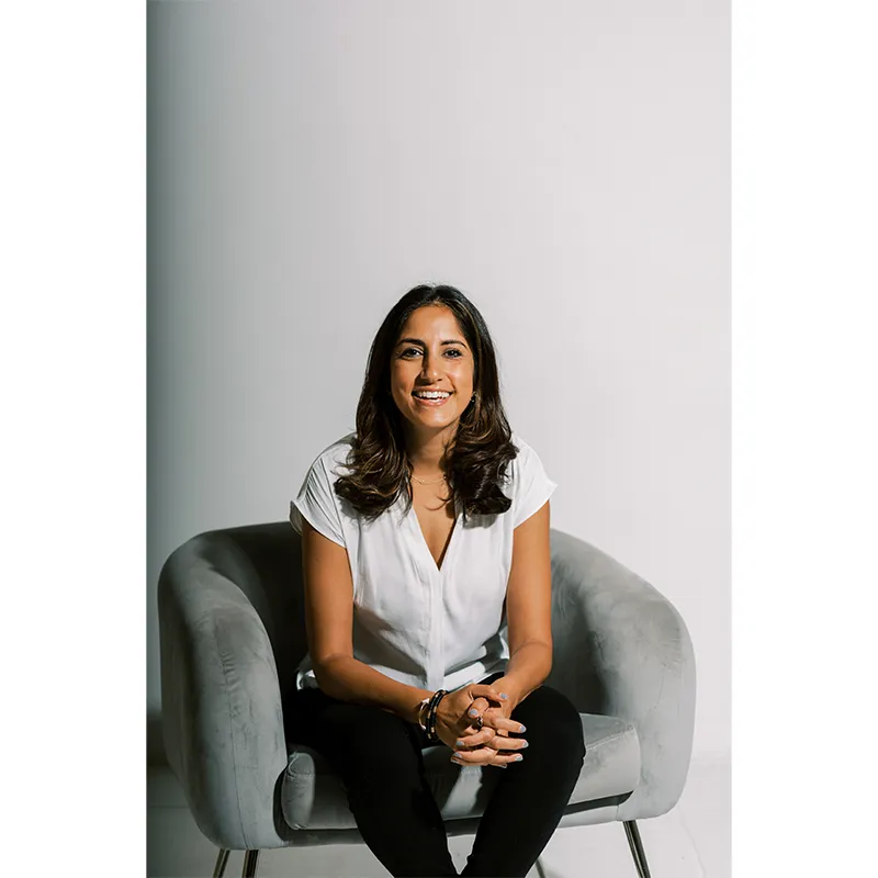 Photo of Rina Hurst sitting on gray chair, white backdrop