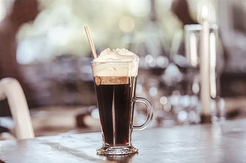 A hot coffee topped with cream in a glass with a straw in it.