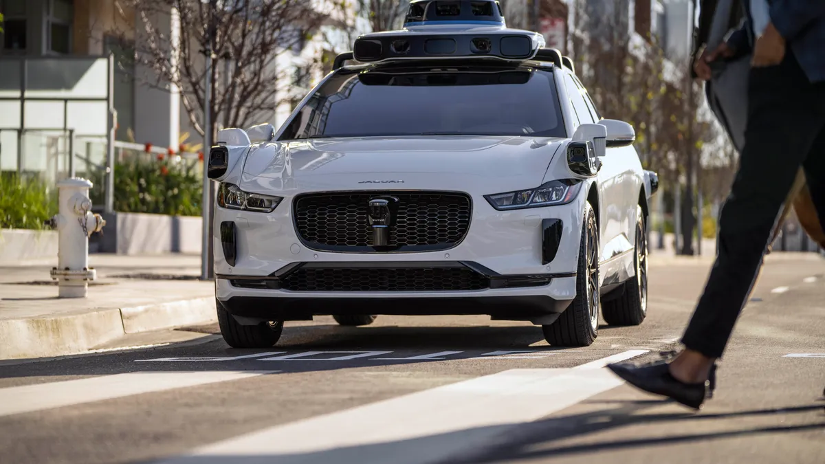 A autonomous Waymo Jaguar I-PACE SUV yields to a pedestrian at a crosswalk.