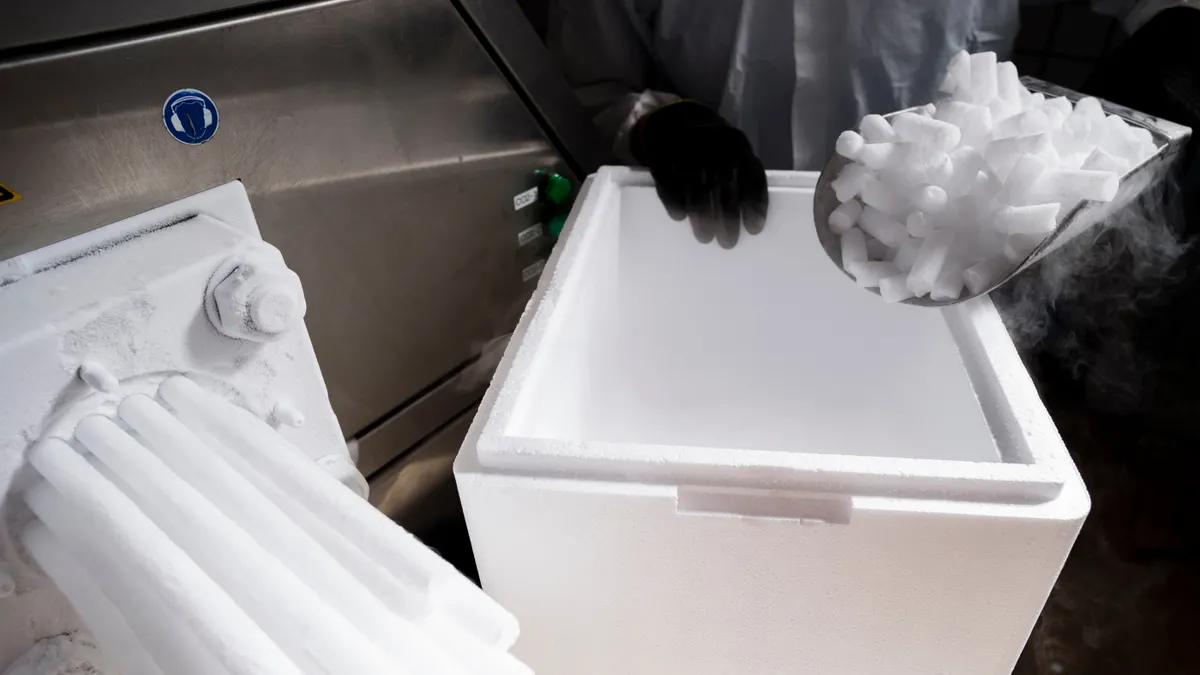 Dry ice is being made from a machine while a person's hands wearing protective gear scoops the dry ice pellets.