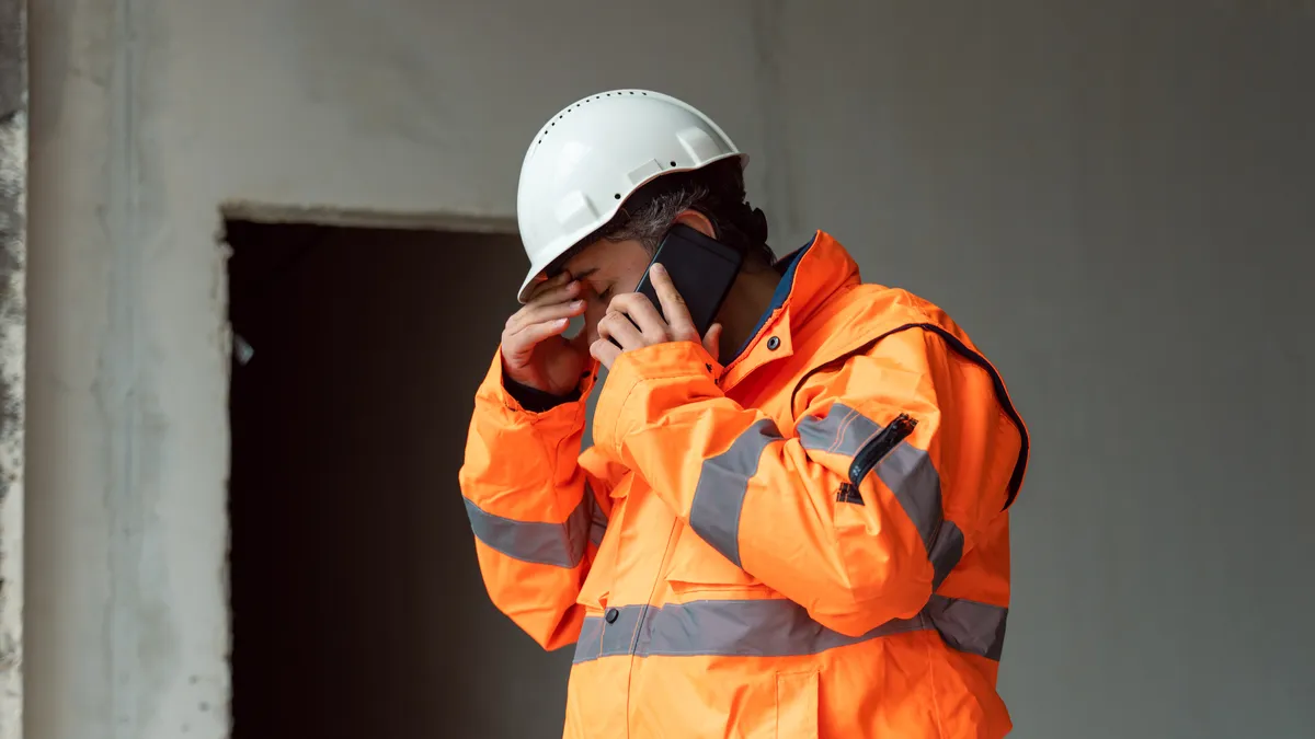 An engineer in a bright vest and hard hat talks on the phone.