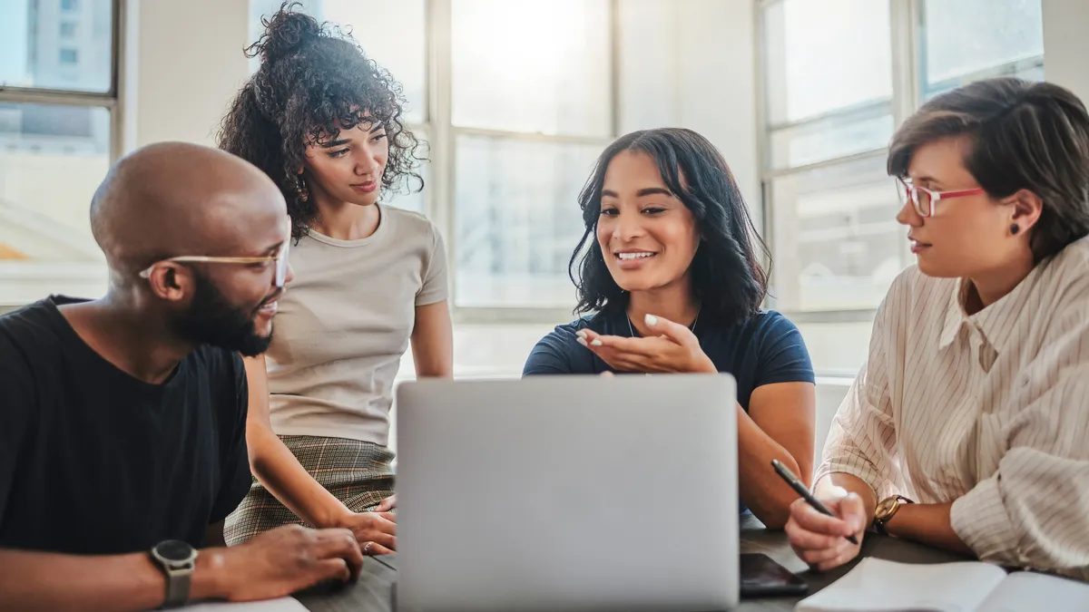 Four people have a discussion in front of a laptop.