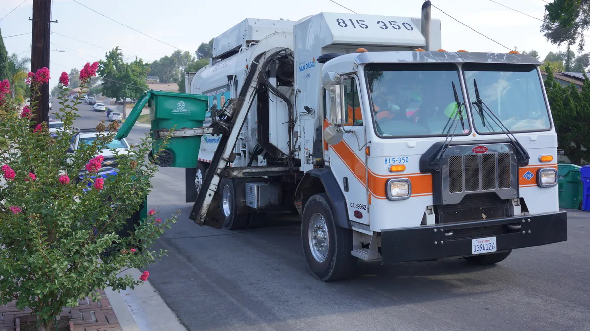 Truck collecting a cart with green waste in San Diego, California, street with parked cars in the background