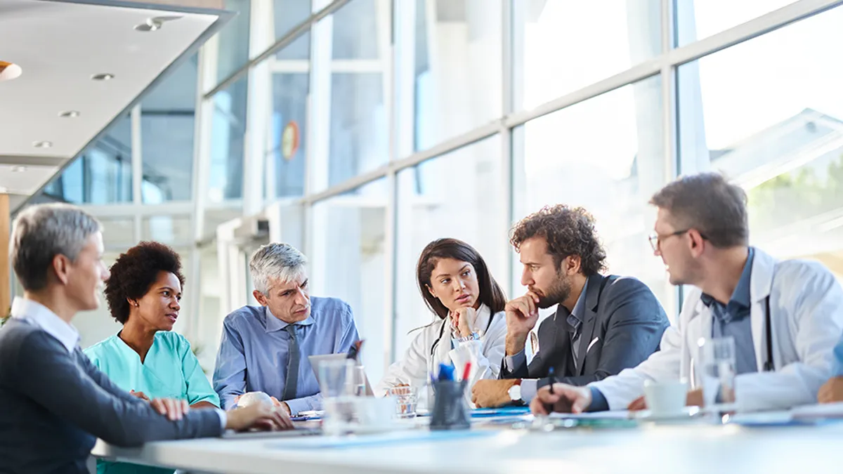 A group of physicians and business workers siting at a table thinking and talking to eachother in an office building