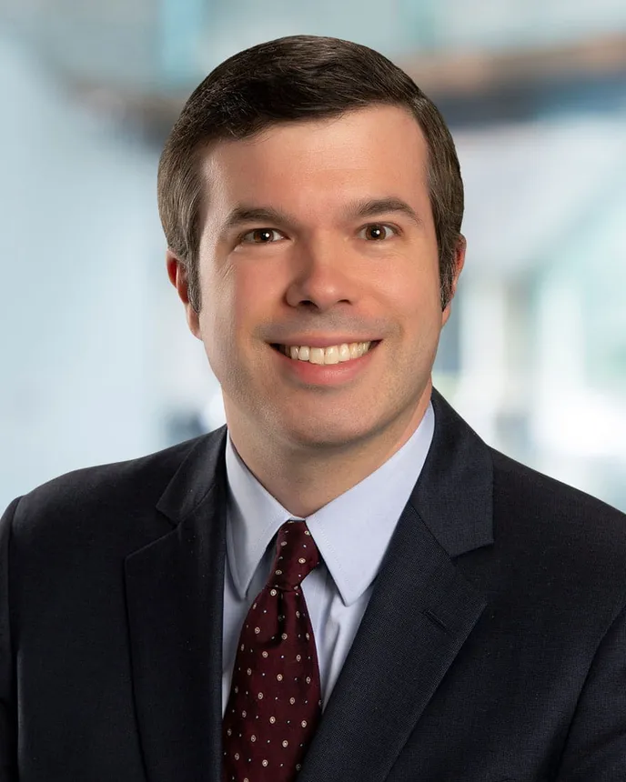 Man with dark hair and brown eyes in a dark suit.