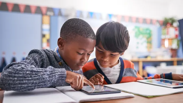 Two elementary students sit together working on a classroom assignment on a tablet.