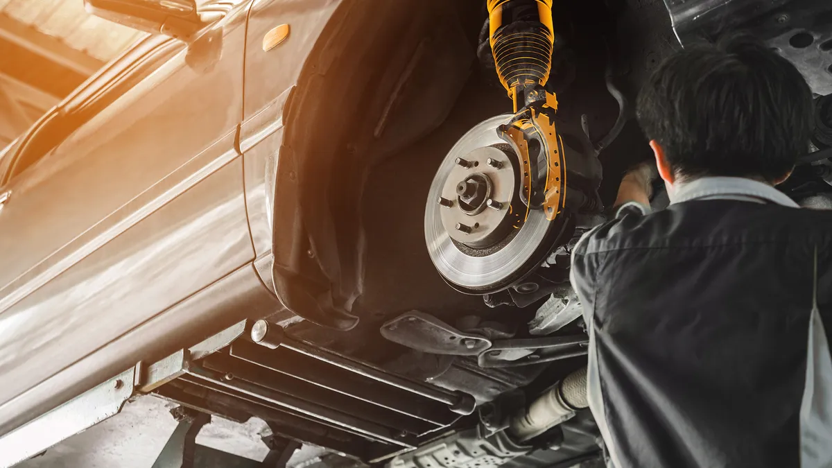 A vehicle on a lift in a repair shop showing a right front air suspension component highlighted in orange for visibility.