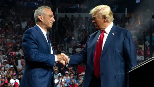 RFK Jr. shakes hands with Donald trump on stage with a crowd behind watching