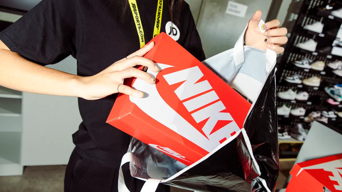 A JD Sports employee puts a Nike shoebox into a bag.