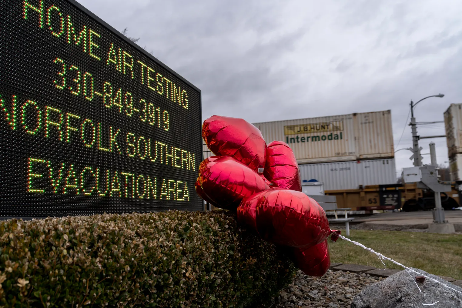 Red balloons are seen next to a digital sign saying residents can receive air-quality tests from Norfolk Southern Railway. In the background, shipping containers can be seen on a train.