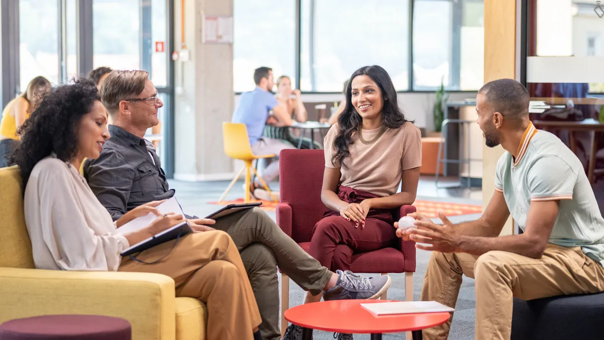 A businessperson talks to a group of diverse business people in a well-lit office