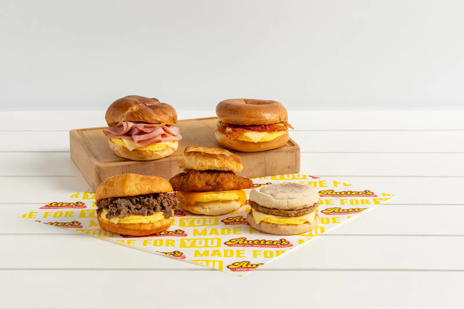 A photo of five brakfast sandwiches on bagels, croissants, biscuits and English muffins and containing a variety of meats, cheese and eggs on a wrapping paper that says &quot;Rutter&#x27;s&quot; against a white background.