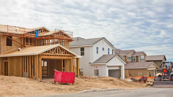 a wood frame on a new house next to two existing houses with a sand front yard
