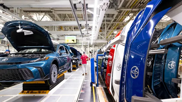 Carmy sedans and move on the assembly line at Toyota Motor Manufacturing Kentucky next to a row of colored front bumpers with Toyota badges.