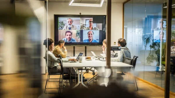 A group of employees attend a hybrid attendance presentation from a small meeting room.