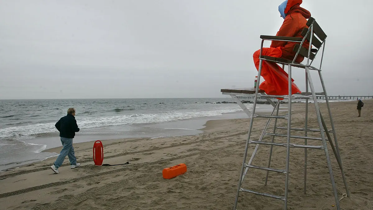 A person jogs along a rainy beach past a lifeguard.
