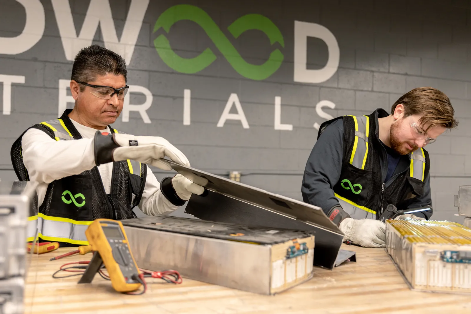 Two employees at Redwood Materials disassemble batteries for recycling.