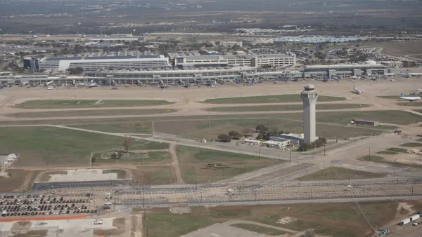 Aerial view of an airport with runways, air traffic control tower, parking lot and other buildings.