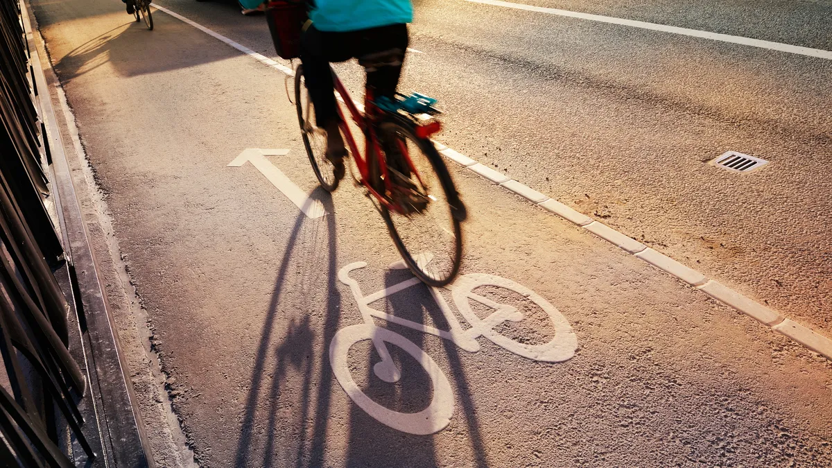 Bike lane in evening. Sign for bicycle painted on the asphalt. Car and traffic in background. Dividing line. Shadow from sunset sun.