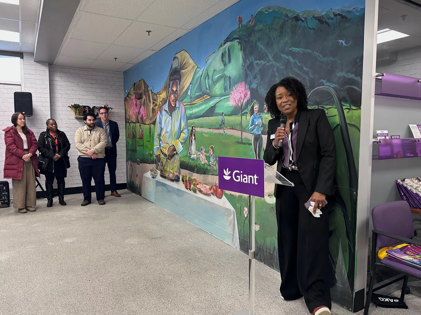 Woman addressing a small gathering in front of a newly debuted mural