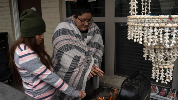 People warm up by a barbecue grill.