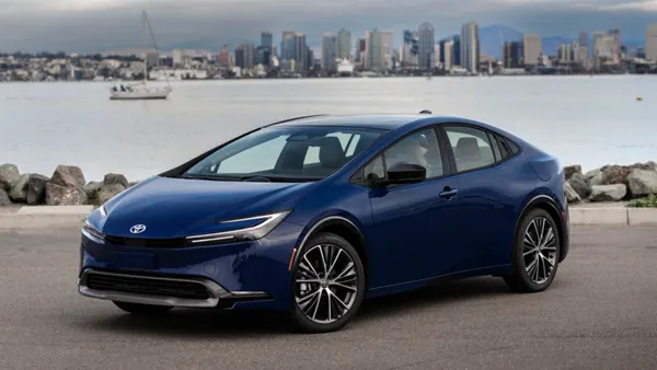 A blue 2024 Toyota Prius parked outdoors with a city skyline in the background.
